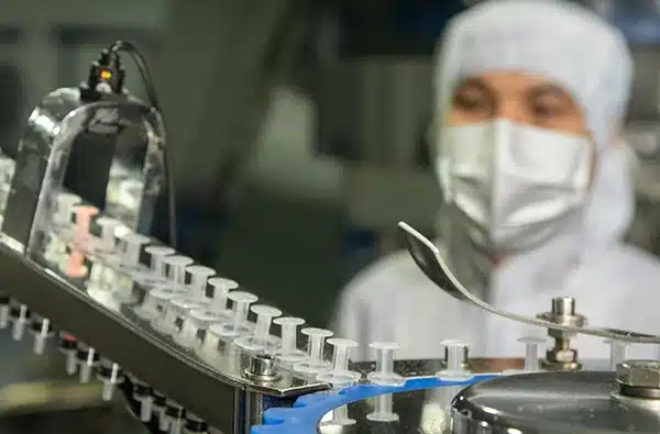 Technician in protective gear working with automated vial filling line at a life-sciences manufacturing facility